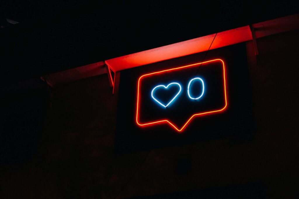 Et neon skilt i mørket som består af en rødfarvet taleboble med et hjerte og et 0 nul i blåfarve.